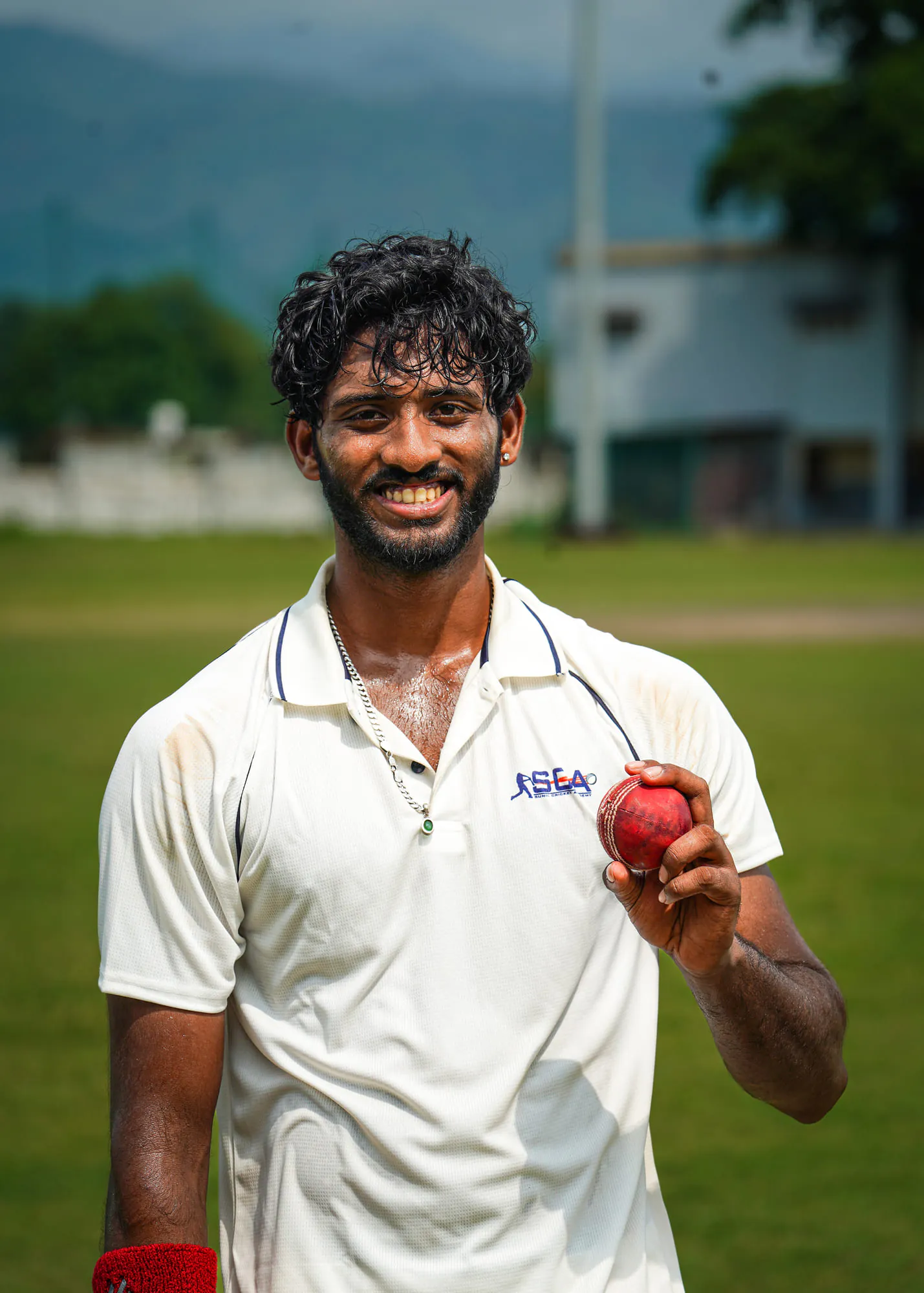 A smiling SCA bowler in whites holding up the red ball
