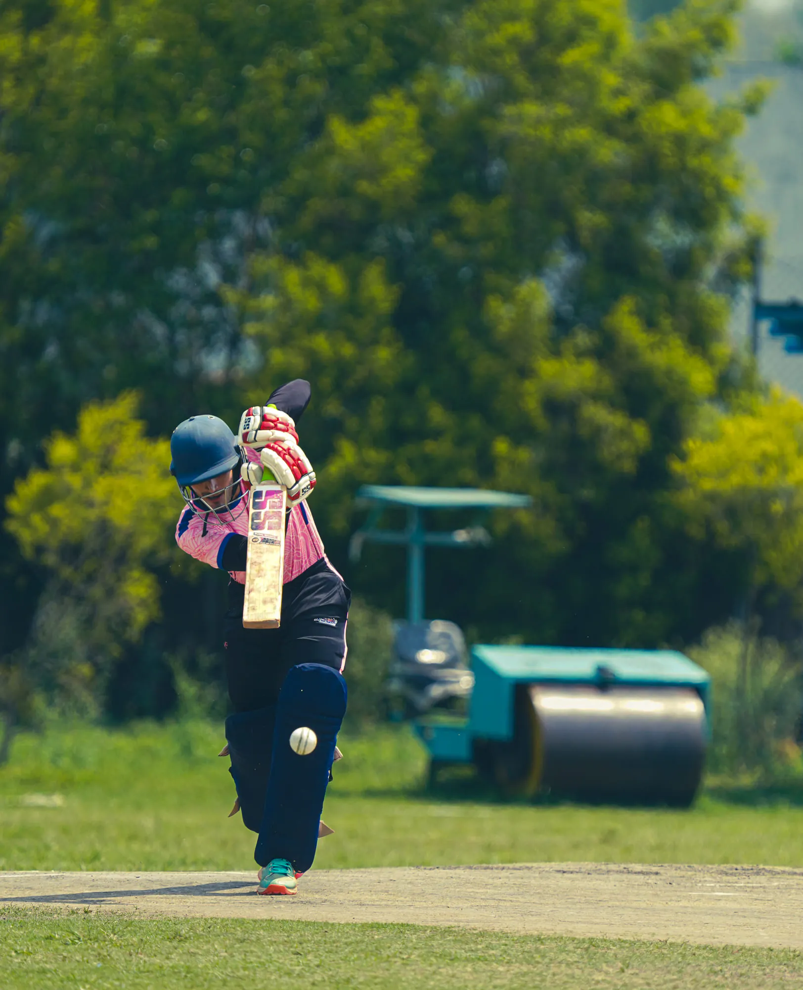A young batter driving the ball on an open ground