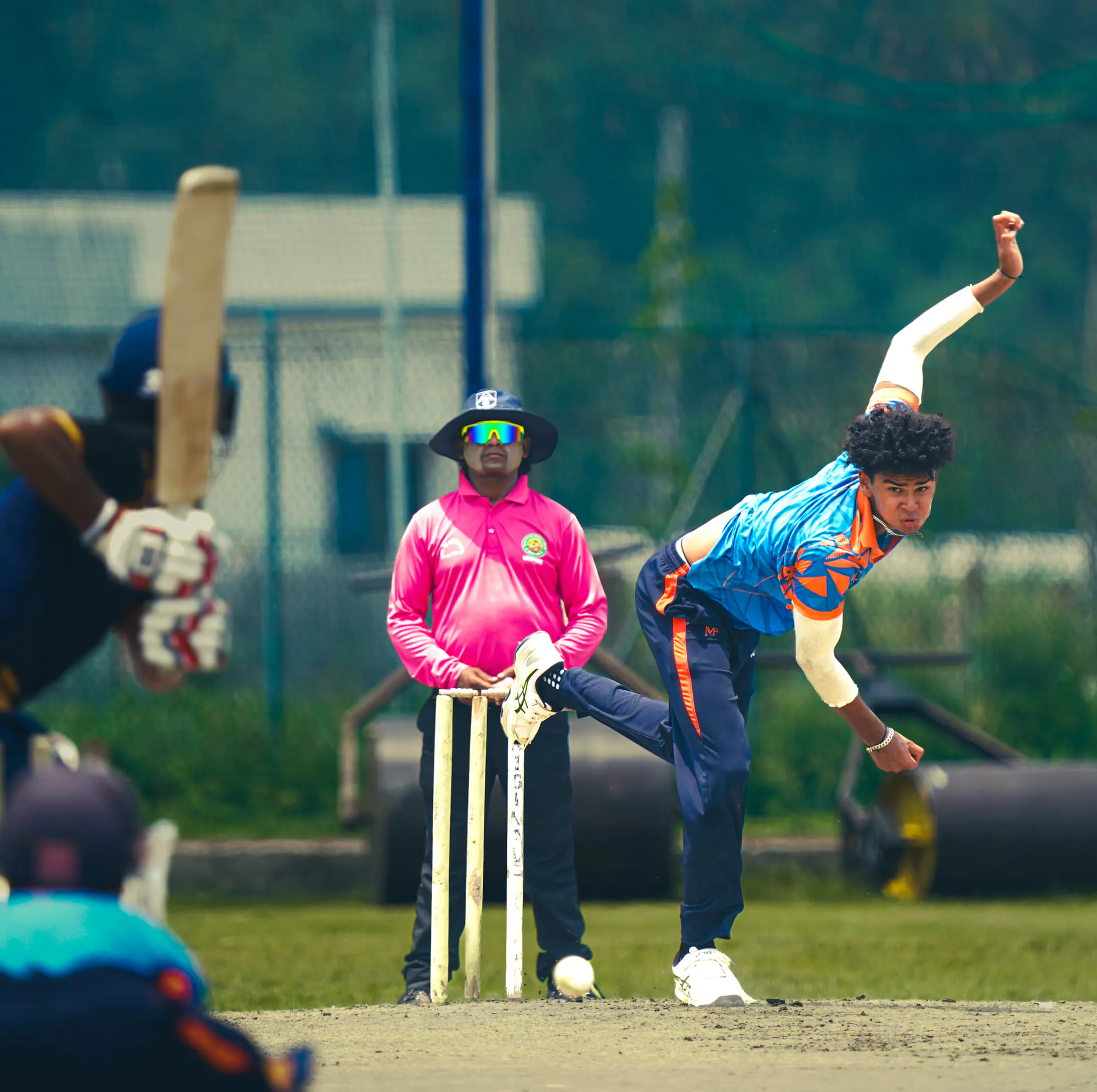 An SCA bowler in full follow-through as the ball pitches in front of the umpire