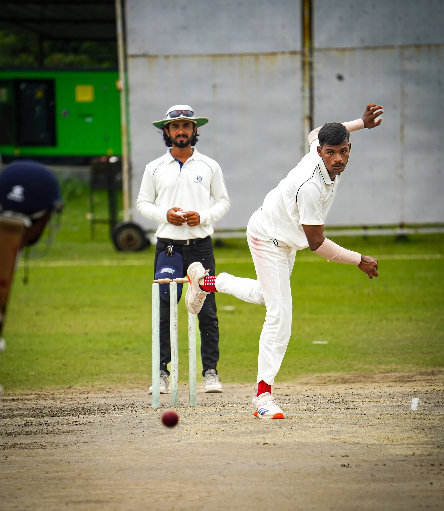 A bowler in whites delivering the red ball during a match