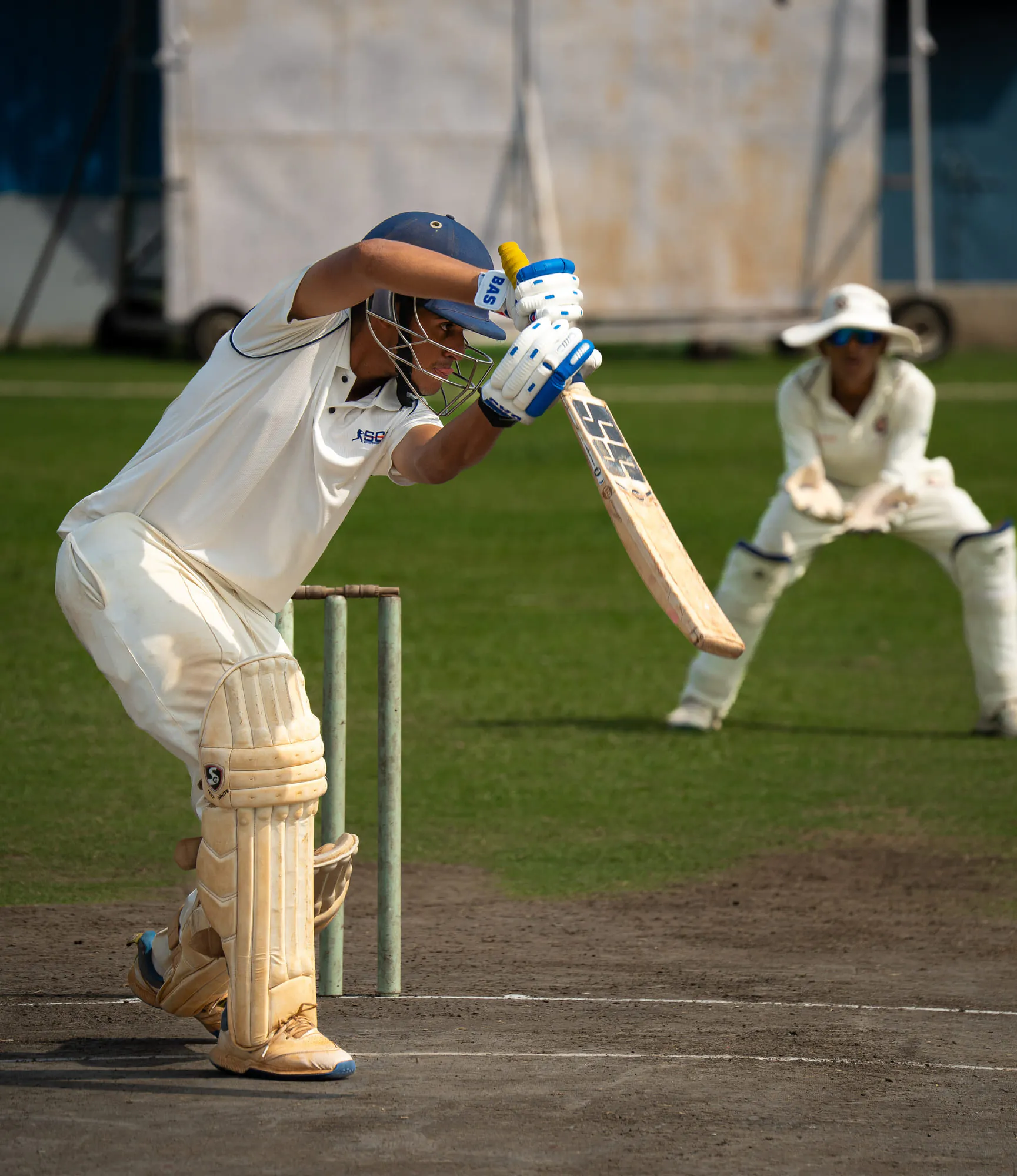 A batter in whites getting into line, the wicketkeeper crouched behind
