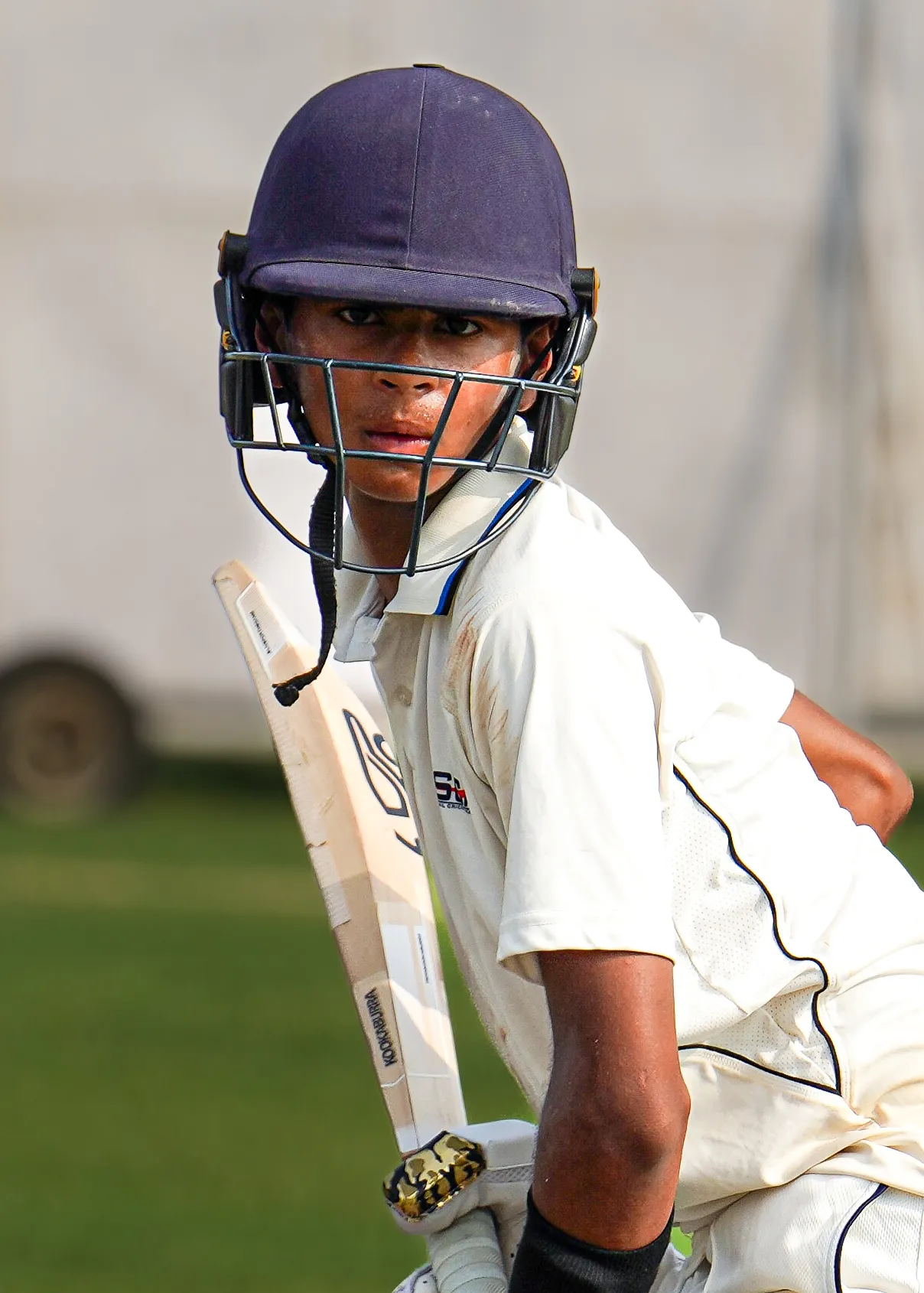 Close portrait of a helmeted batter in whites looking down the pitch