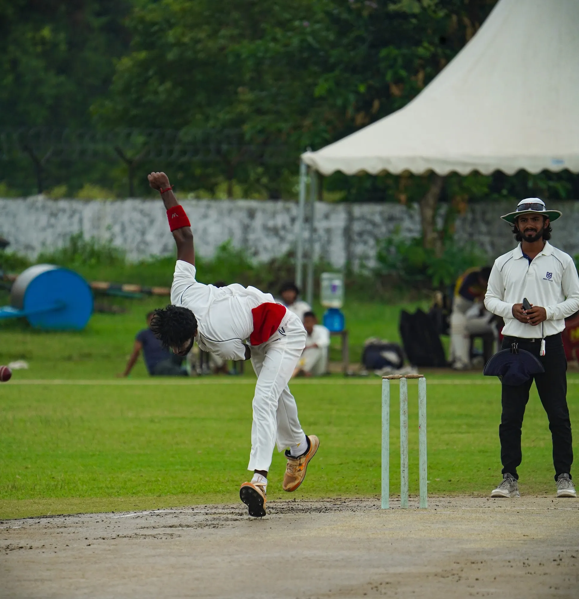 A bowler in whites bent low in his follow-through