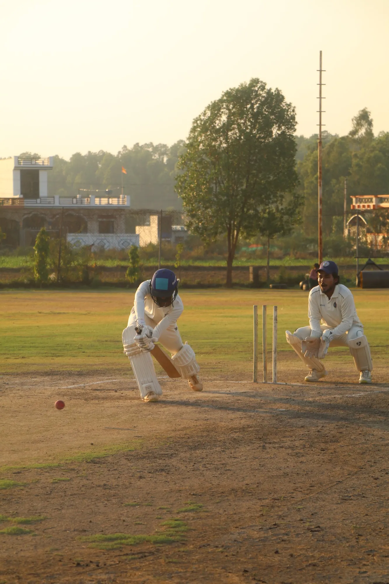 A batter and wicketkeeper crouched at the crease at dusk
