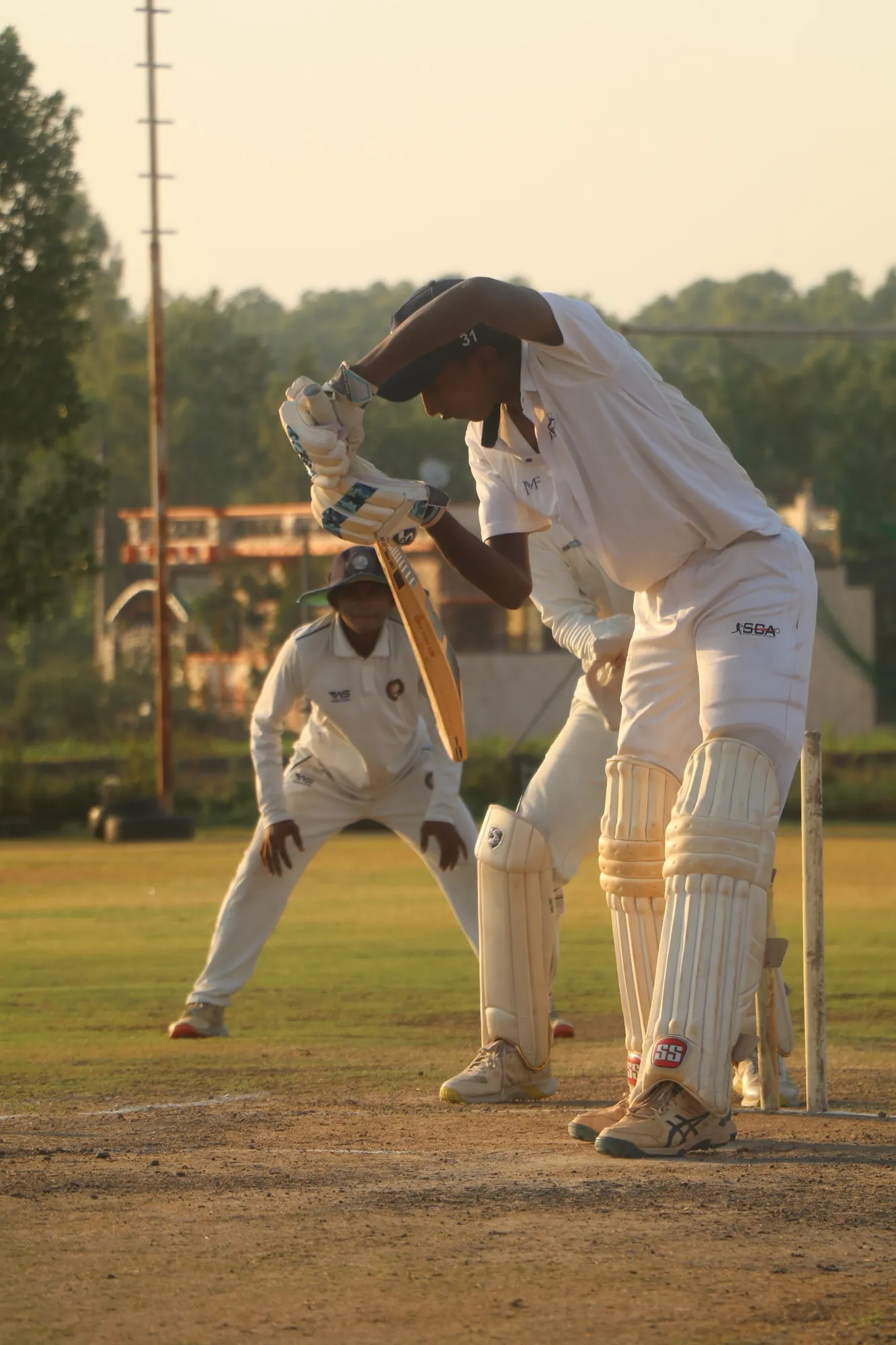 A batter in whites defending in evening light