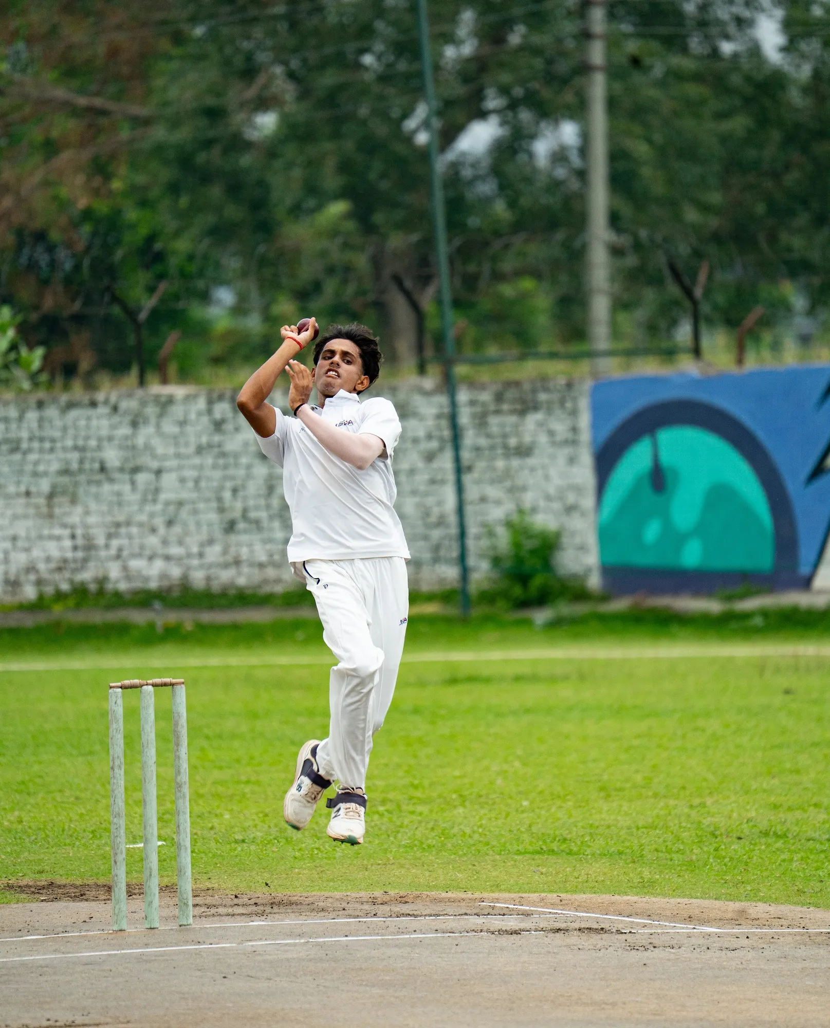 A bowler in whites leaping into his gather