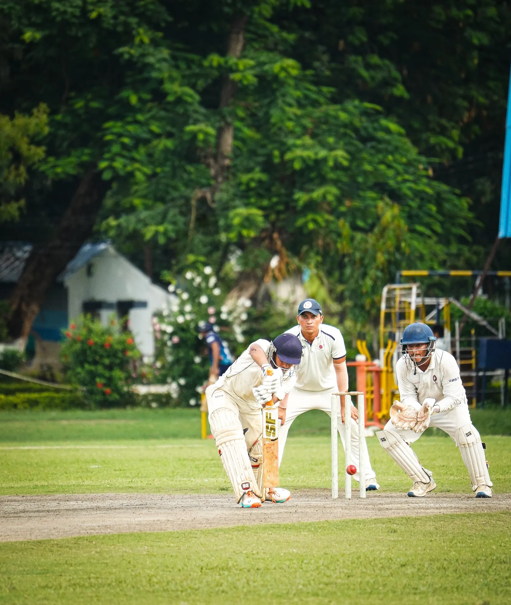 A batter in whites defending with the wicketkeeper and slip behind him