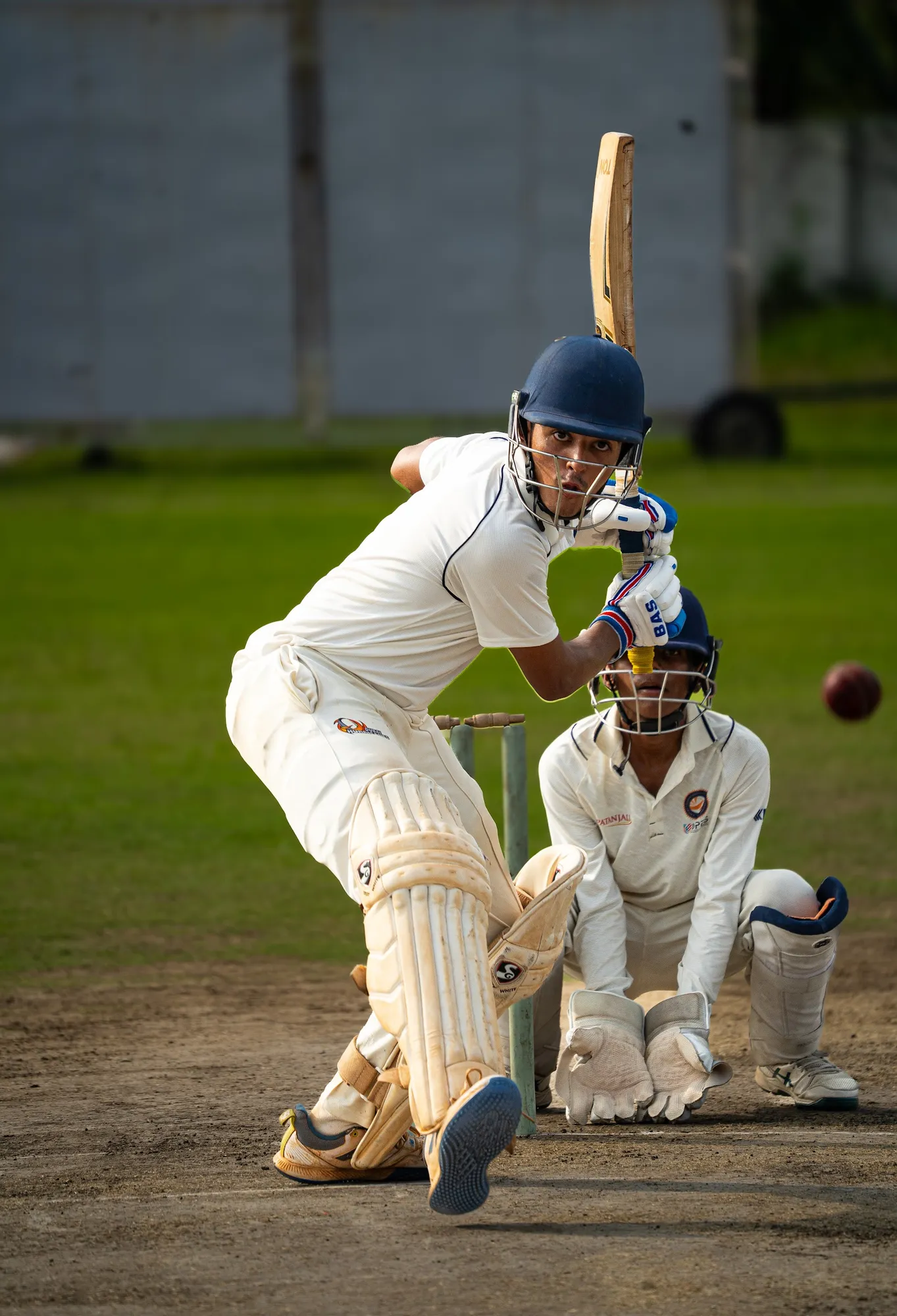 A batter in whites swaying out of the line of a rising red ball