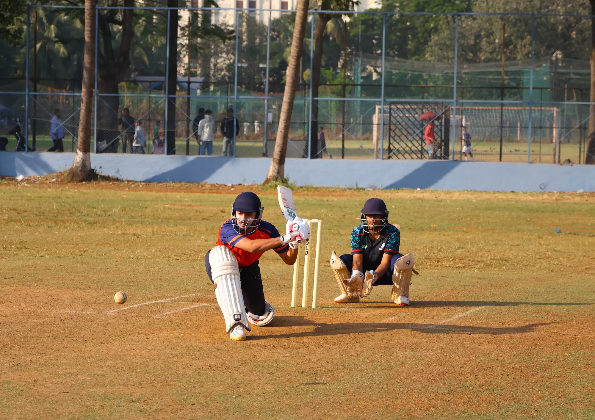 A batter down on one knee sweeping, the wicketkeeper crouched behind