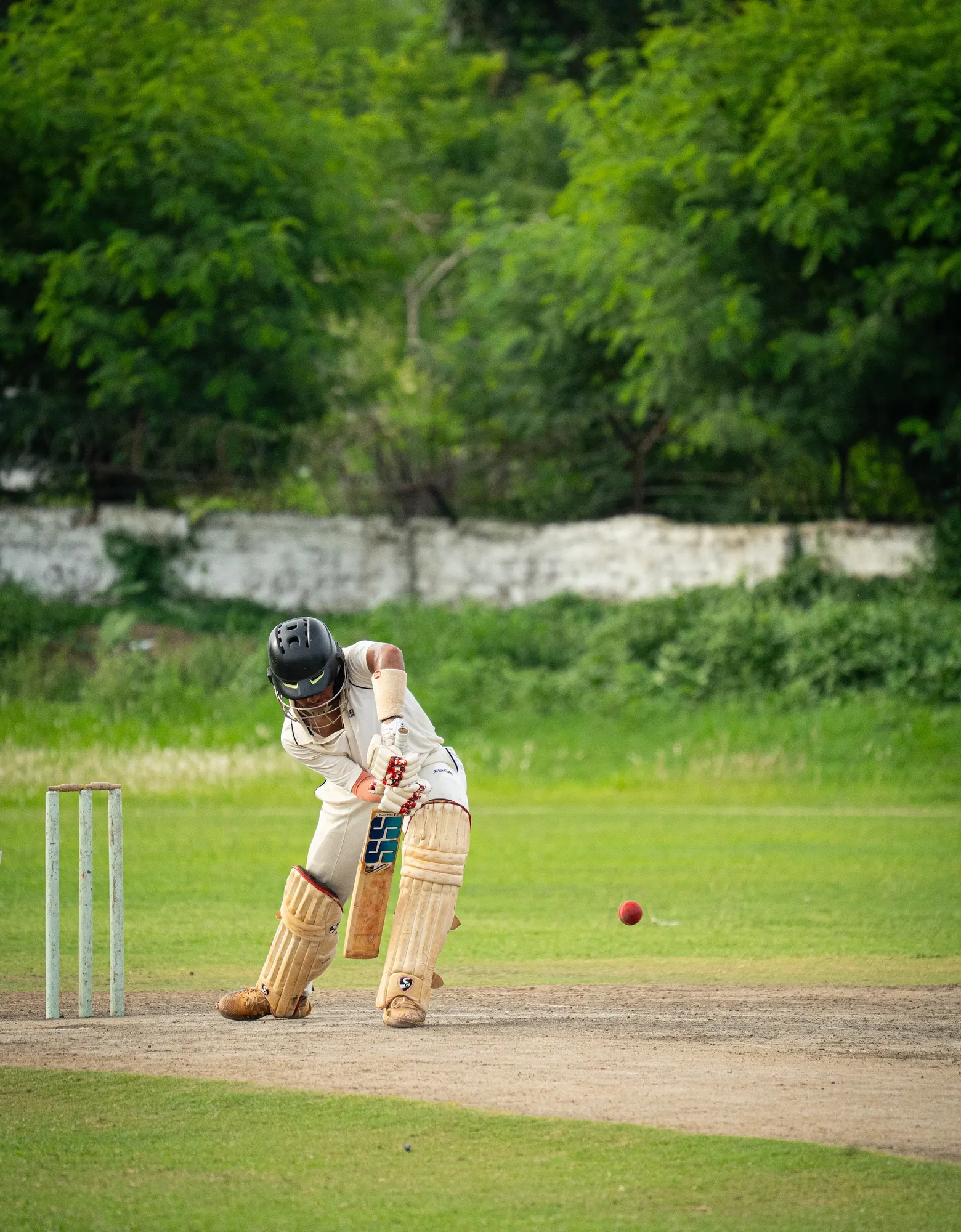 A batter in whites watching the red ball on to the bat