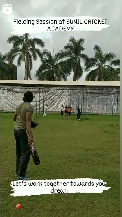 A coach with a bat hitting catches to players spread across the academy ground.