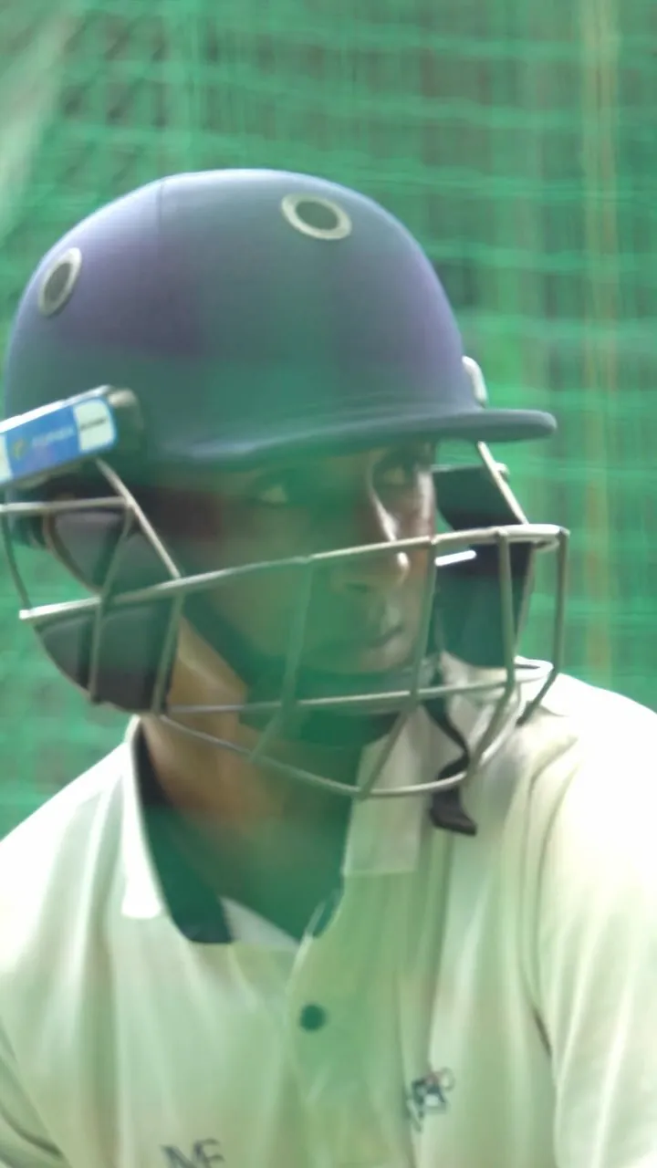 Sagar Gupta in cricket whites and a batting helmet, seen through the net at a practice session.