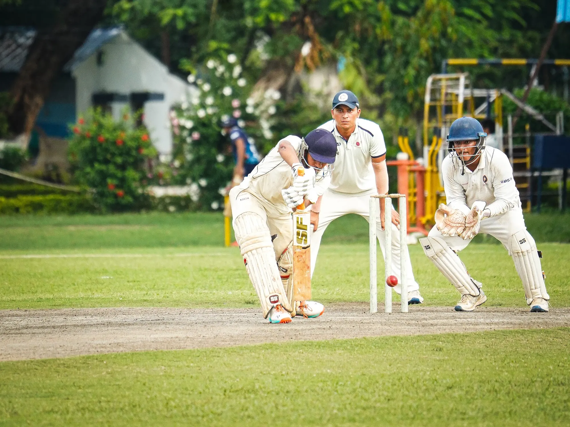 A batter in whites defending with the wicketkeeper and slip behind him