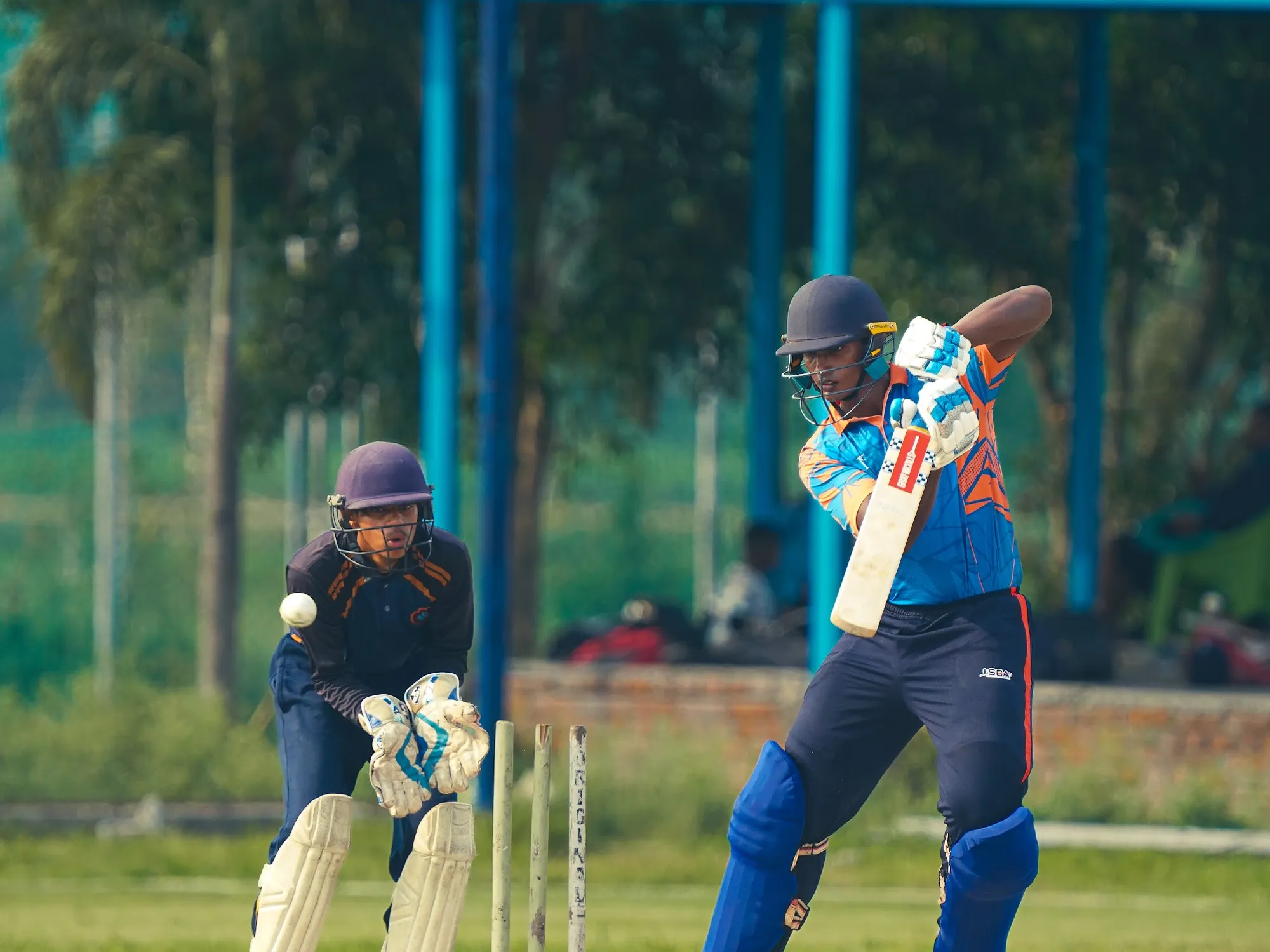 A batter shaping to play as the wicketkeeper waits behind the stumps